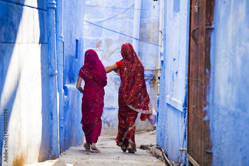 Obraz na płótnie Two women dressed in the traditional Indian Saree are walking through the narrow streets of the blue city of Jodhpur, Rajasthan, India. w salonie