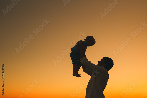 Father and son silhouettes at sunset on a sea beach. © nataliaderiabina