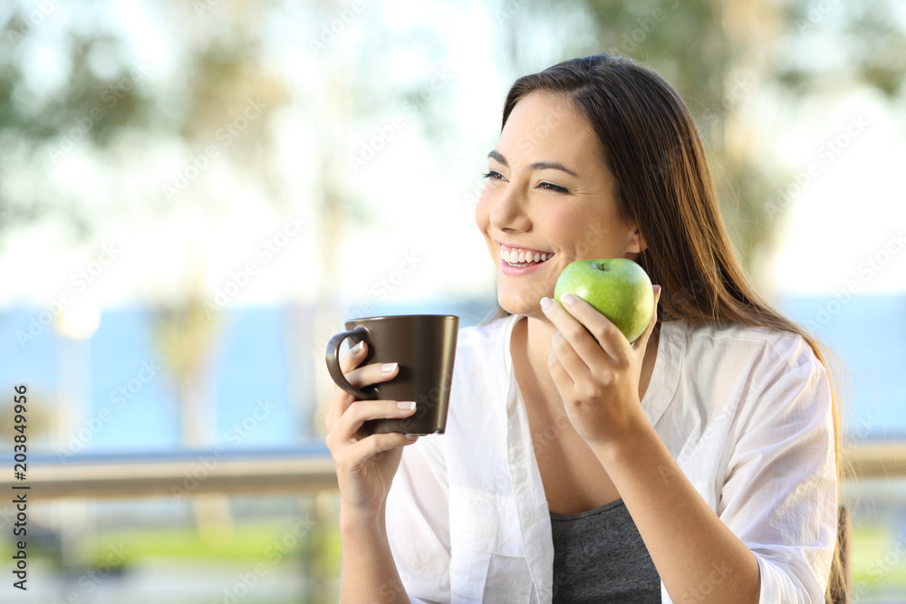 Happy woman holding an apple and a coffee mug Happy woman holding an apple and a coffee mug