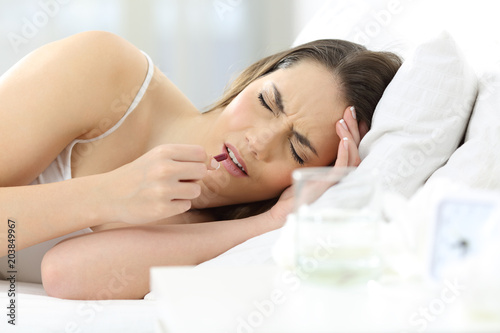 Ill woman taking a painkiller pill on the bed at home