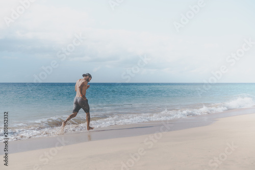 Workout exercise concept.Healthy Handsome Active Man With Fit Muscular Body running on the beach on the morning. Sporty Athletic Male Exercising At Beach. Training Outdoor. Sports And Fitness Concept.