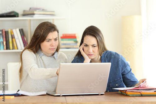 Two worried students consulting online information in a laptop