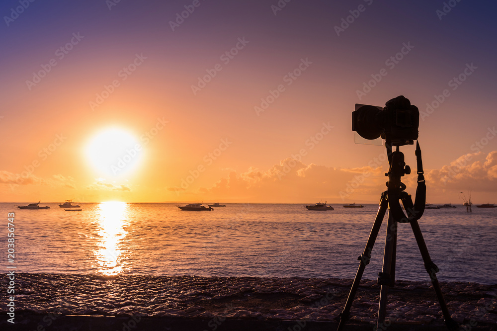 silhouette of camera on tripod shooting sea with sunset.