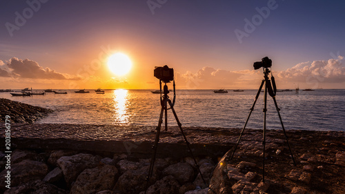 silhouette of camera on tripod shooting sea with sunset.
