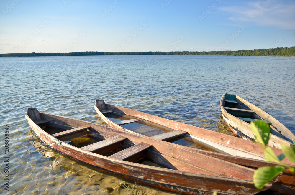 Old wooden fishing boats on the lake beach with blue sky.