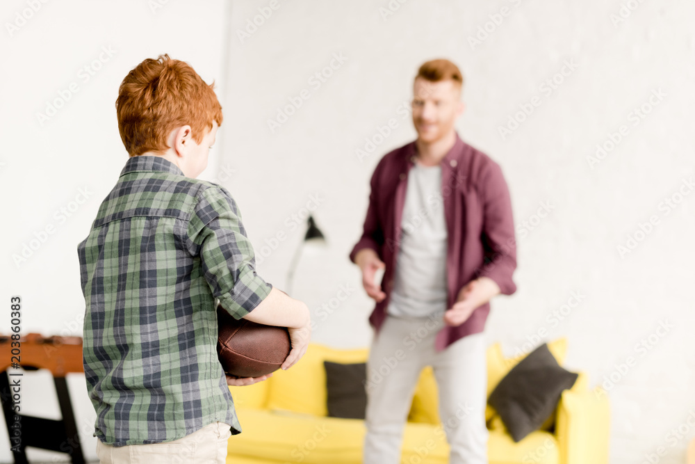 Obraz premium redhead father and son playing with rugby ball at home