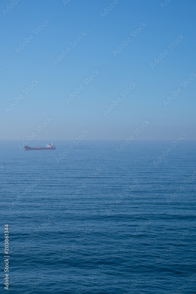 Cloudy horizon and Fog over the sea waves, natural background, red cargo ship on the horizon