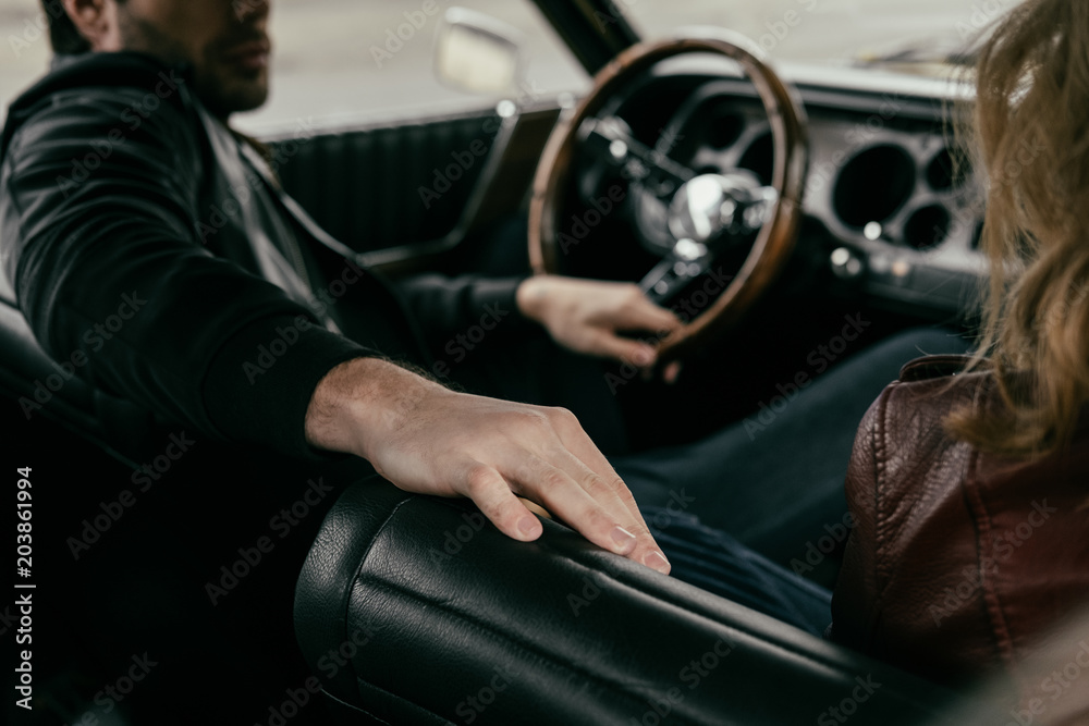 Naklejka premium cropped shot of young man and woman sitting in retro car