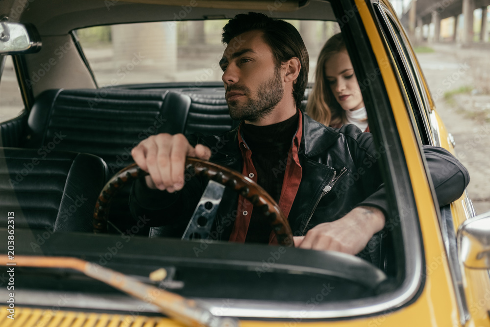 Obraz premium handsome young man driving retro car and girlfriend sitting behind