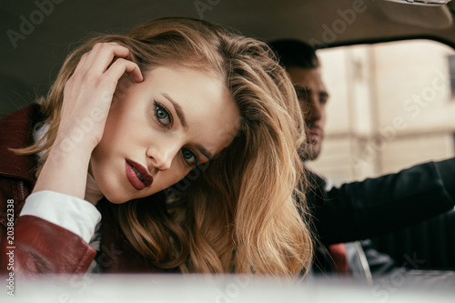 beautiful stylish young woman looking at camera while boyfriend driving car