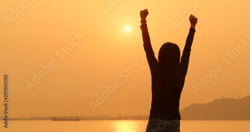 Woman raising hand up under sunset
