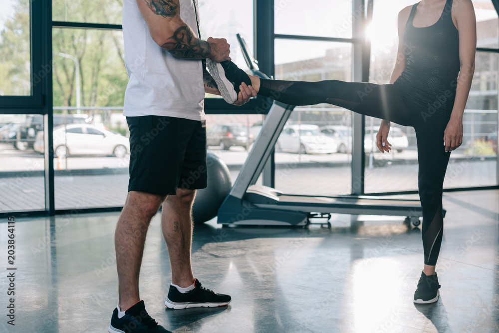male personal trainer helping sportswoman to stretching at gym male personal trainer helping sportswoman to stretching at gym