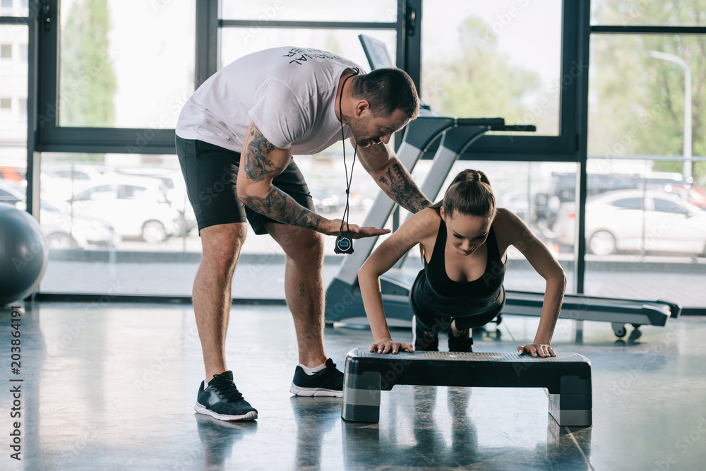 Fototapeta male personal trainer helping sportswoman to do push ups at gym