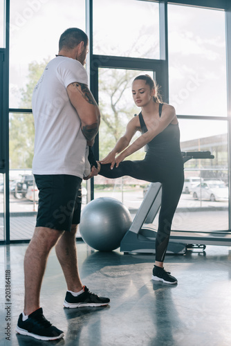 male personal trainer helping sportswoman to stretching at gym