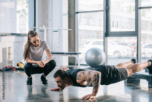 female personal trainer looking at sportsman doing push ups at gym