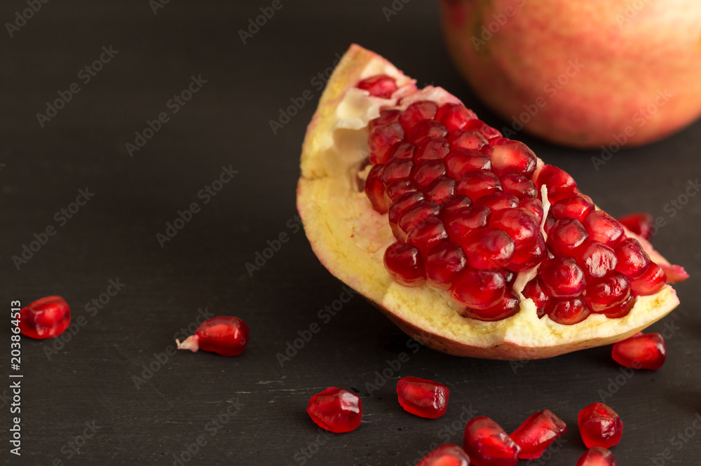 Pomegranate fruit slice and seeds still life on rustic black background Pomegranate fruit slice and seeds still life on rustic black background