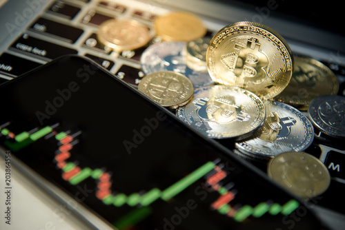 Bitcoin gold silver coins and smartphone with basic candlestick green red graph price screen on laptop keyboard. Close up and focus on Bitcoin. Worldwide cryptocurrency and digital payment concepts