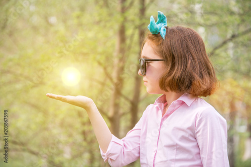 girl in a pink shirt and sunglasses in the nature holding a sun photo