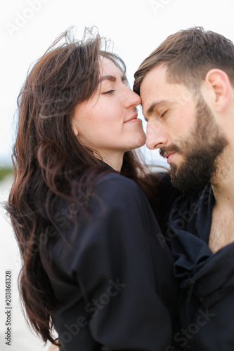 Close up beautiful woman hugging man in white monophonic background, wearing black shirt. Concept of romantic love and seaonal winter photo session, fashion and clothes collection. photo