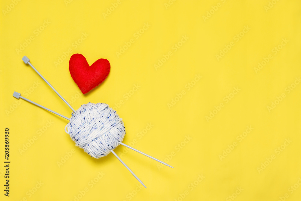 Top view of yarn and red felt heart on yellow background, love to knit image concept Top view of yarn and red felt heart on yellow background, love to knit image concept