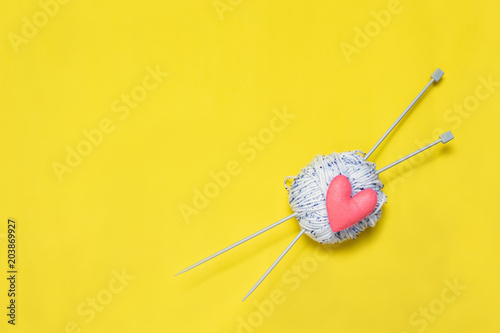 Top view of yarn and red felt heart on yellow background, love to knit image concept