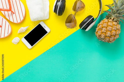 Summer Holidays background Concept, Phone with pineapple, glasses and flip flops On a green and yellow background top view