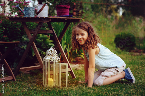 dreamy romantic kid girl relaxing in evening summer garden decorated with lantern and candle holder lights. photo