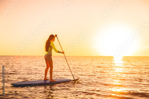 Sporty girl stand up paddle surfing with beautiful sunset or sunrise colors