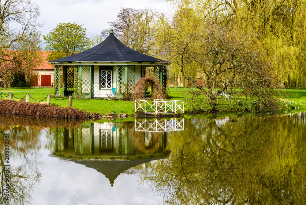 Vittskovle, Sweden. White and black gazebo with reflections in motionless water on a cloudy spring day.