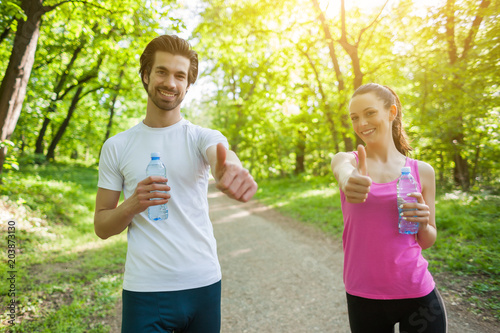 Young couple exercising in park. They are drinking water. 