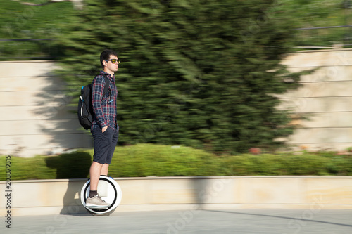  A stylish guy moves along the sidewalk on a mono-wheel.
