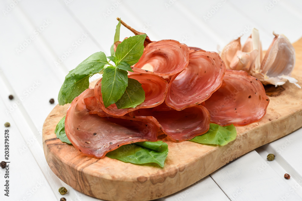 Salami smoked sausage slices basil leaves and peppercorns on white background Salami smoked sausage slices basil leaves and peppercorns on white background