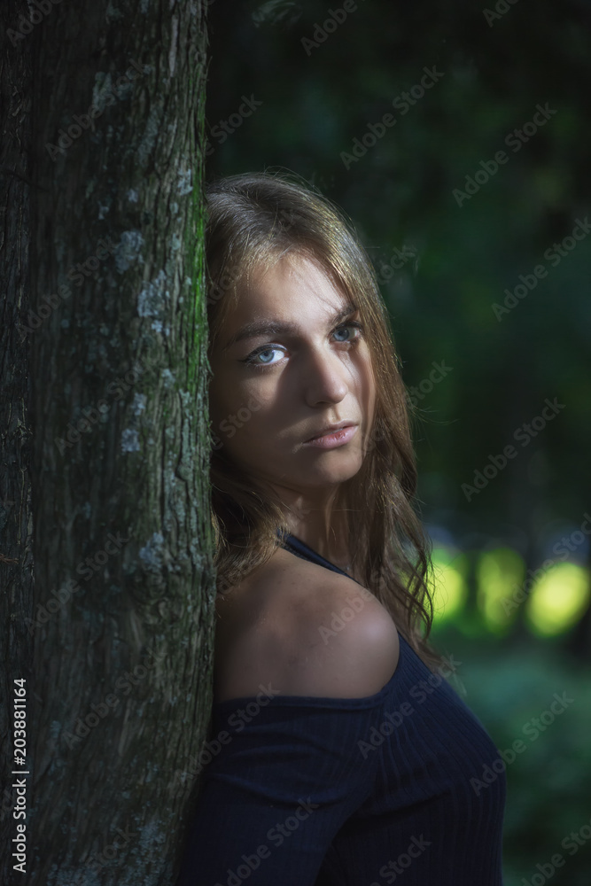 Sad girl standing by the tree trunk Sad girl standing by the tree trunk
