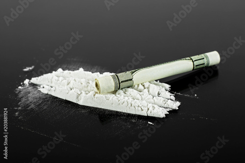 Rolled hundred dollars banknote and pile of cocaine on black background, closeup