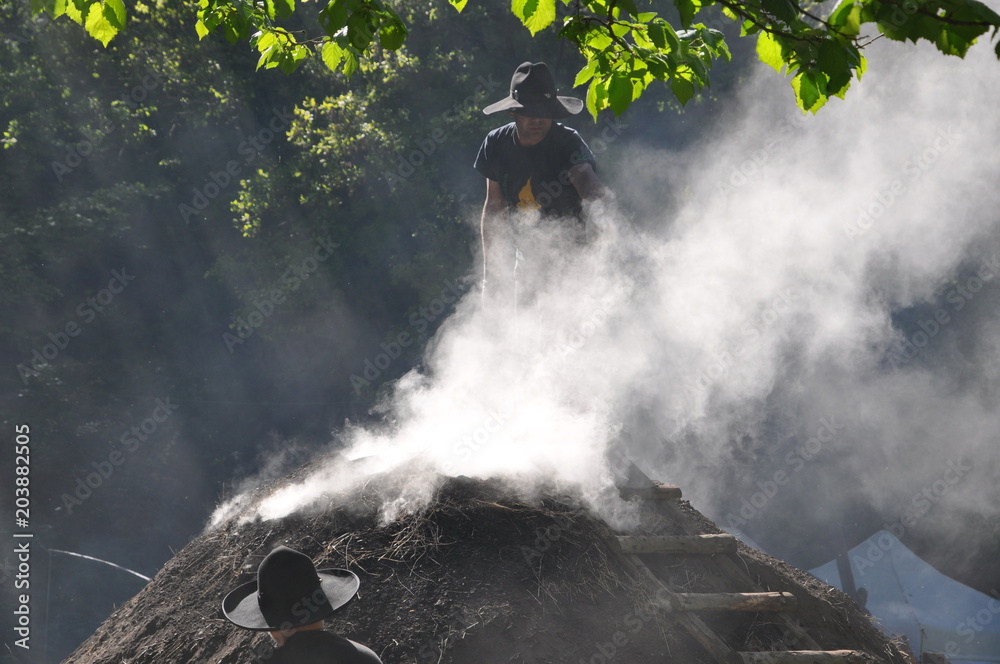 Fototapeta premium Köhler arbeitet am traditionellen Holzkohlemeiler zu Herstellung von Holzkohle aus Buchenholz