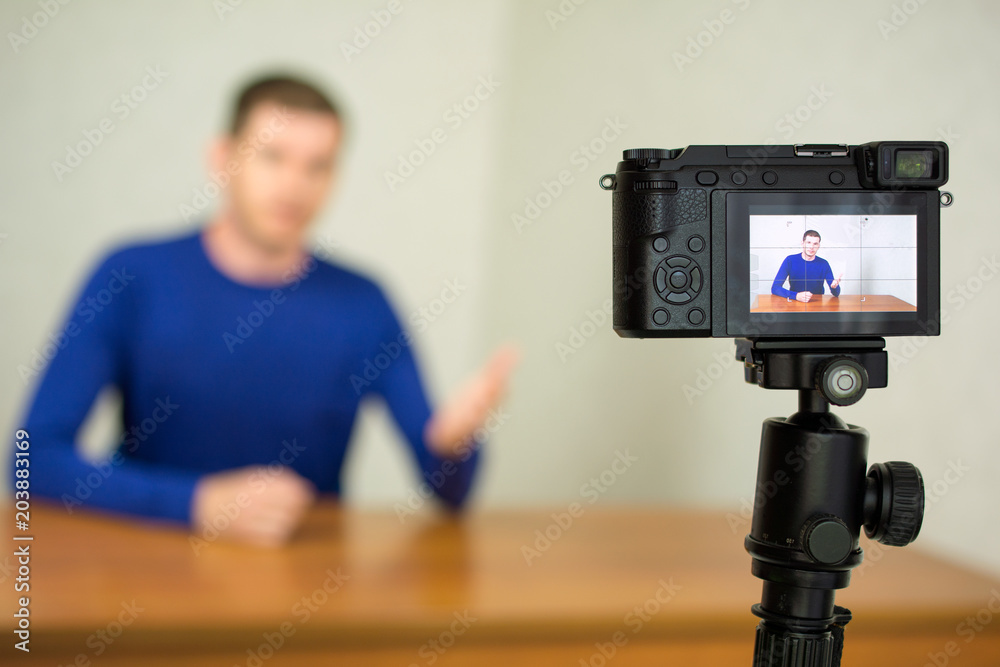 Young male blogger recording video at home using a tripod mounted digital camera