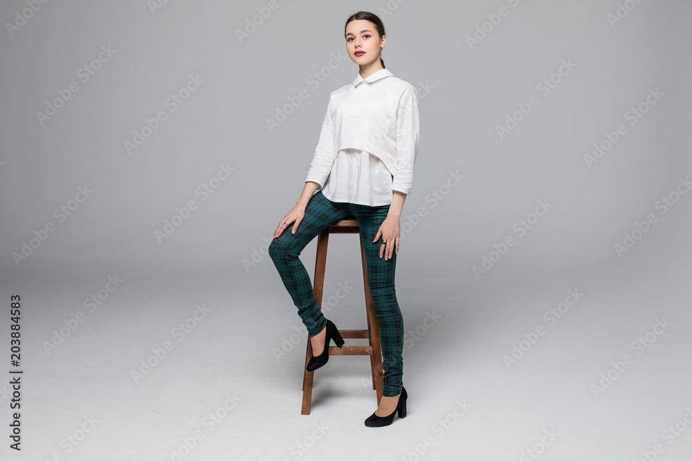 Full length portrait of a young woman sitting on chair over gray background Full length portrait of a young woman sitting on chair over gray background