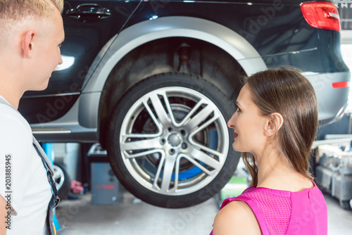 Beautiful woman looking happy at a handsome and reliable young auto mechanic, after tuning her car with new cool rims in a trendy automobile repair shop © Kzenon