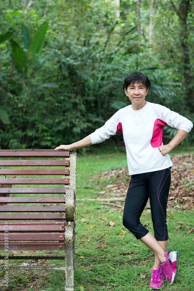 Asian senior woman standing beside park bench