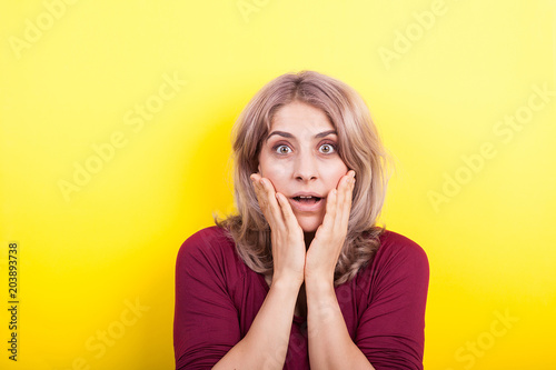 Beautiful blonde woman surprised on yellow background in studio photo