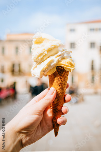 Woman's hand holding italian ice cream in waffle cone on summer light.