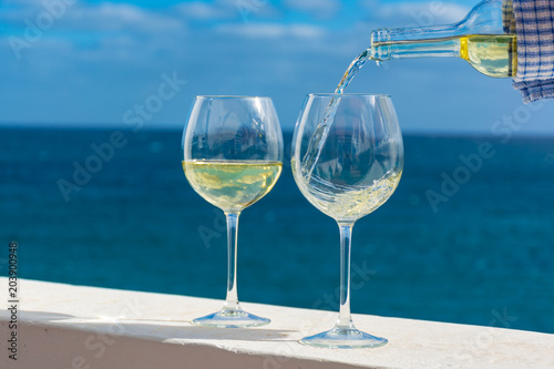 Waiter pouring glass of white wine on outdoor terrace with sea view