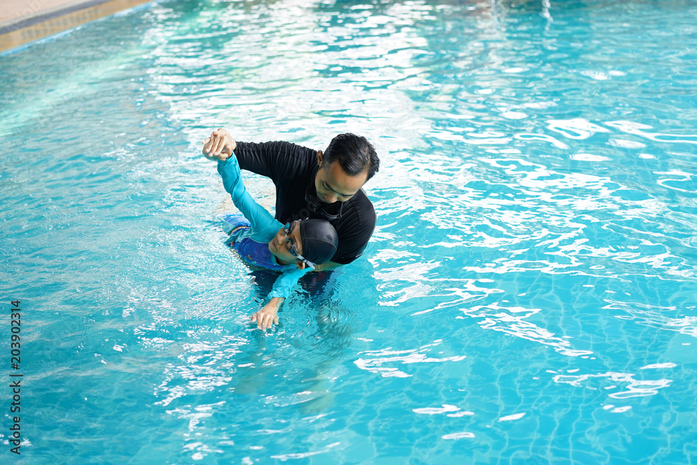 Father teaching daughter to swim in a swimming pool