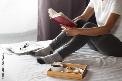 girl enjoying a book with coffee on the bedroom in the morning
