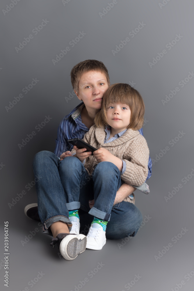 Happy mother and her 4 years old little son dressed in denim sitting together on grey background for studio shoot
