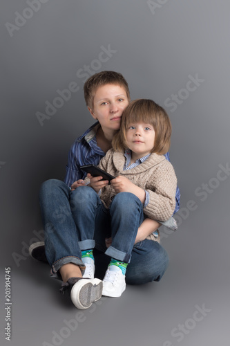 Happy mother and her 4 years old little son dressed in denim sitting together on grey background for studio shoot