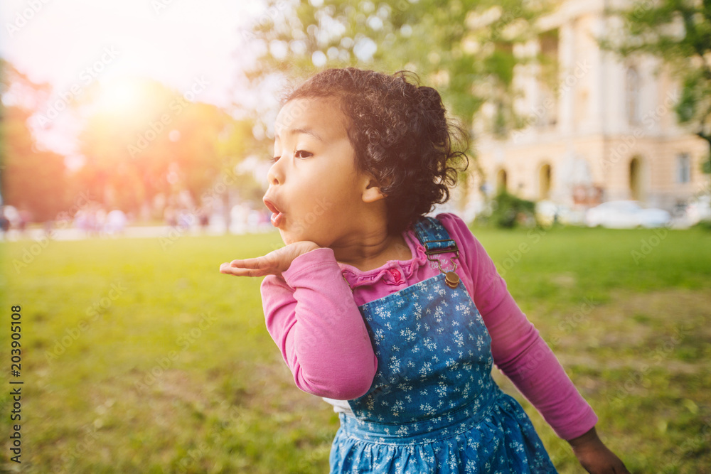 Cute curly mexican dark skinned toddler baby girl sends an air kiss in european city square. Growing up, leadership, copying female psychology behavior concept. Cute curly mexican dark skinned toddler baby girl sends an air kiss in european city square. Growing up, leadership, copying female psychology behavior concept.