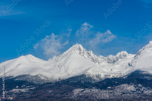 Slovakia: Big Tatras (Vysoke Tatry) on the spring. Big mountains with the snow and clouds. The lake in foreground. Small village near the mountain and hill.