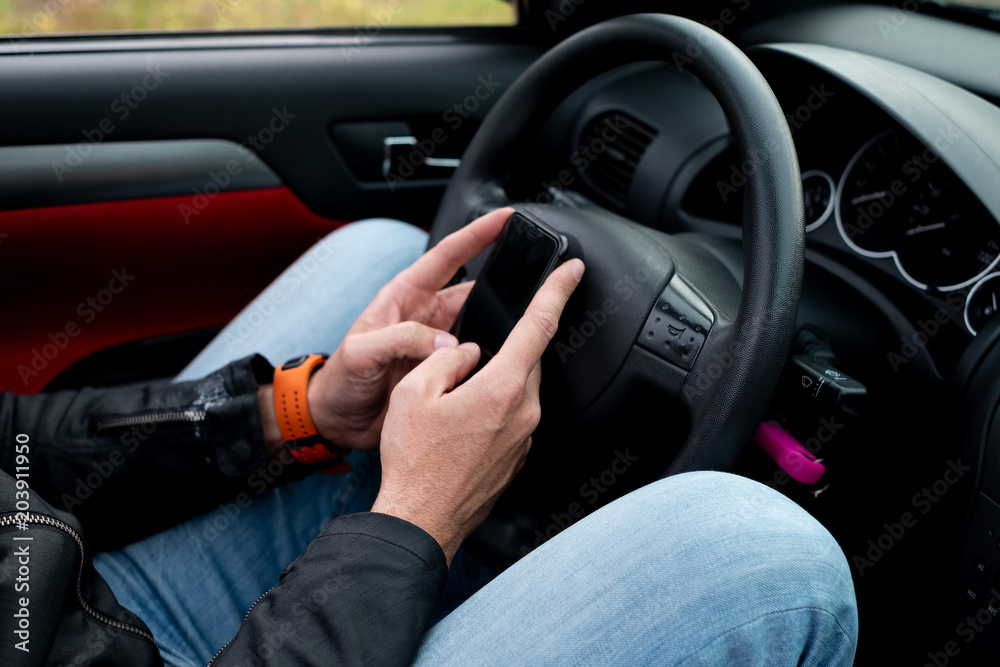 Men's hands on his cell phone on the mobile phone in front of the steering wheel of a convertible car Men's hands on his cell phone on the mobile phone in front of the steering wheel of a convertible car