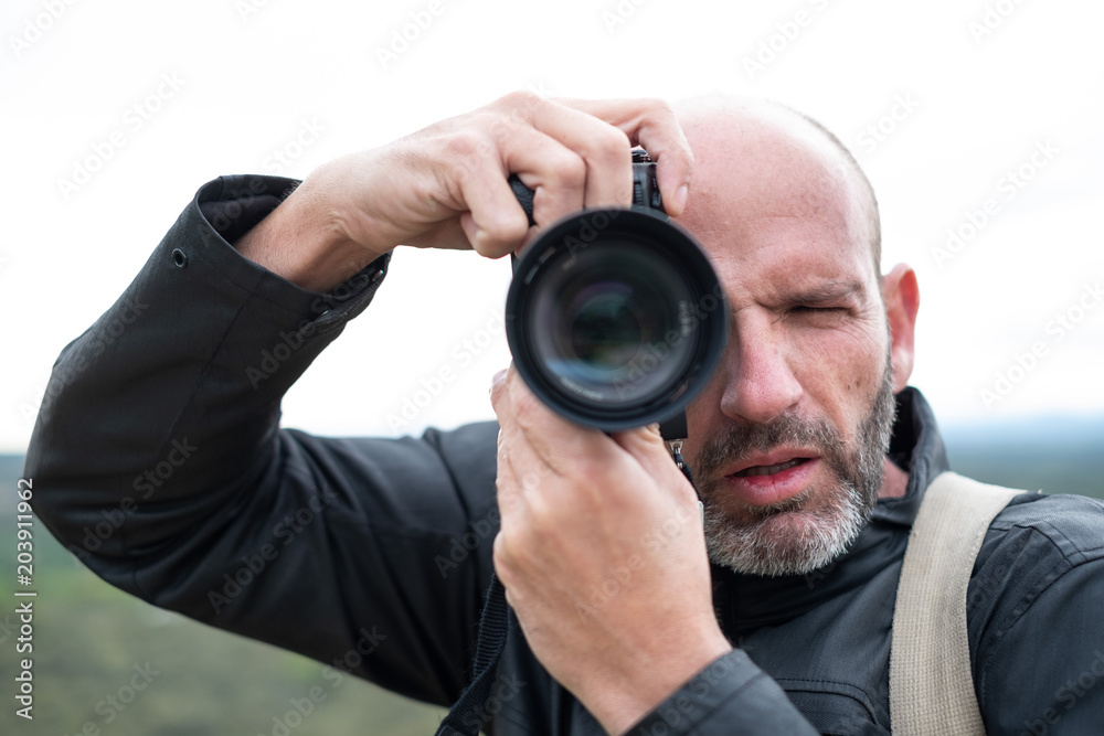Portrait of a middle-age bald photographer with beard and leather jacket taking pictures at work with digital camera on the countryside Portrait of a middle-age bald photographer with beard and leather jacket taking pictures at work with digital camera on the countryside